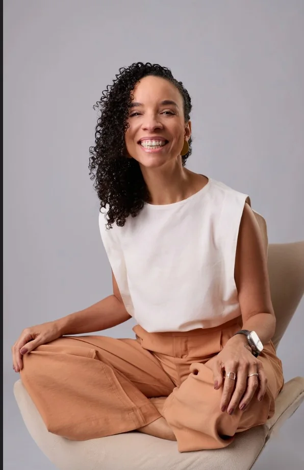 Renata Lage, psicóloga, sorrindo em retrato profissional com blusa branca e calça coral